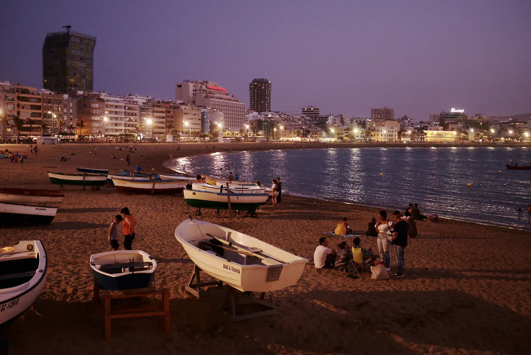 La playa de Las Canteras, en Las Palmas de Gran Canaria, al anochecer: barcas en la arena y las terrazas del paseo ya iluminadas.